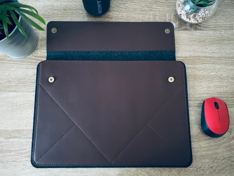 May include: A brown leather laptop sleeve with a flap closure and a soft grey felt lining. The sleeve has gold-coloured metal snaps and a stitched diamond pattern.