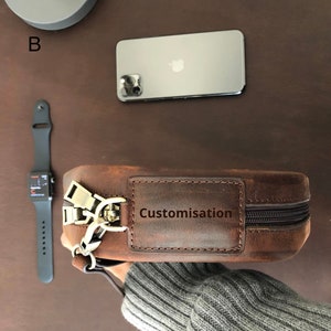 May include: A brown leather bag with a zipper closure and a brass buckle. The bag has a small rectangular patch on the front that says "Customisation".