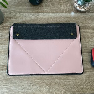 May include: A pink laptop sleeve with a grey felt flap and two gold metal poppers. The sleeve has a stitched diamond pattern and a black border.