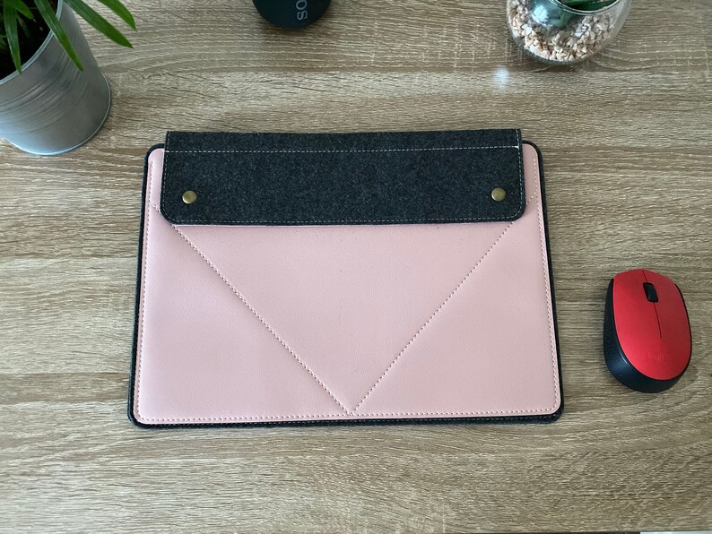 May include: A pink laptop sleeve with a grey felt flap and two gold metal poppers. The sleeve has a stitched diamond pattern and a black border.