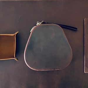 May include: A set of four brown leather goods, including a small tray, a camera case, a camera strap, and a notebook cover.