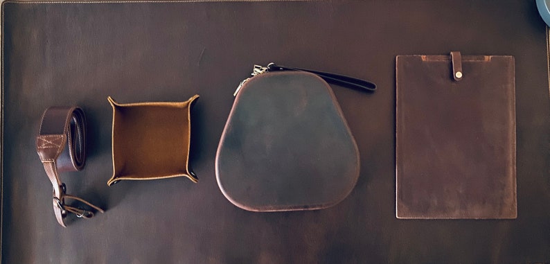 May include: A set of four brown leather goods, including a small tray, a camera case, a camera strap, and a notebook cover.