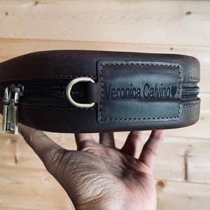May include: A brown leather zippered pouch with a personalized name tag that reads "Veronica Calvino" with a heart symbol.