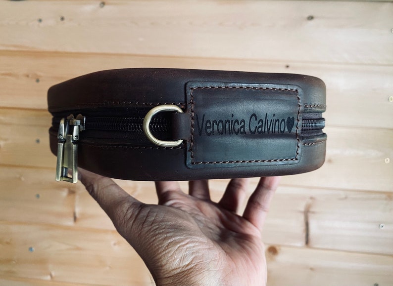May include: A brown leather zippered pouch with a personalized name tag that reads "Veronica Calvino" with a heart symbol.