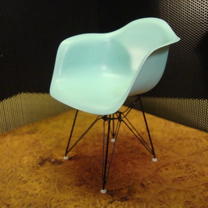 May include: A light blue plastic chair with a black metal frame. The chair has a curved back and a wide seat. The chair is sitting on a wooden surface.