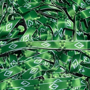Può includere: Un mucchio di cordini verdi con disegni geometrici bianchi e la lettera "G". I cordini hanno una finitura satinata e chiusure in plastica nera. Il design include una serie di piccoli cerchi e una forma a diamante.