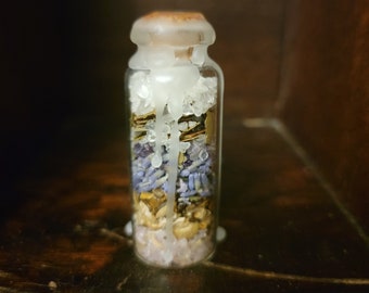 May include: A small glass jar filled with layers of dried herbs, crystals, and white wax. The jar has a cork lid and is filled with a variety of natural ingredients.