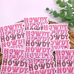 May include: A stack of pink and white stickers with the word "HOWDY" repeated multiple times. The stickers have a leopard print pattern and a star design.