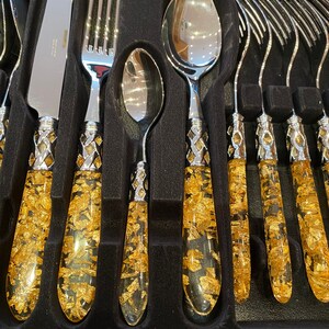 May include: Set of gold-leaf handled silverware, including a knife, fork, spoon, and four smaller forks. The handles are clear and filled with gold leaf flakes.