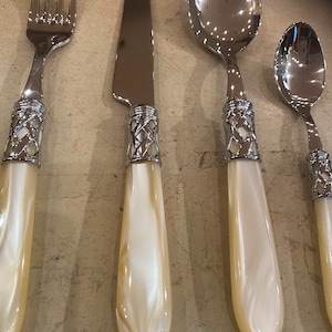 May include: Set of four silver-plated flatware with white pearlescent handles. The set includes a fork, knife, soup spoon, and teaspoon.