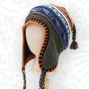 May include: A knit earflap hat featuring a multi-colored geometric pattern in shades of olive green, navy blue, orange, and white. The hat includes long braided tassels hanging from the earflaps and a matching braided tassel at the crown.