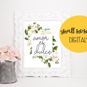 May include: A white floral print with the text "amor es dulce" in black lettering. The text is surrounded by a white frame. The print is in a white frame with a decorative design. The print is on a white background. The text "muy muy dulce" is below the main text.