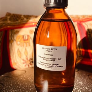 Könnte beinhalten: Eine braune Glasflasche gefüllt mit einer klaren Flüssigkeit, beschriftet mit "COLLOIDAL SILVER 21ppm". Das Etikett enthält Gebrauchsanweisungen, mit Messungen in Pfund und Tropfen. Die Flasche hat einen schwarzen Deckel.