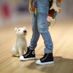 May include: A white stuffed dog sits next to a doll wearing blue jeans and black high-top sneakers.