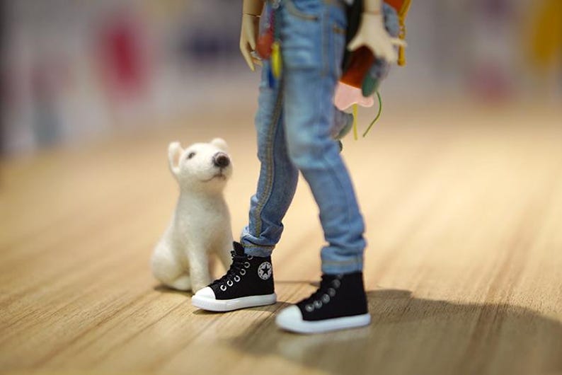 May include: A white stuffed dog sits next to a doll wearing blue jeans and black high-top sneakers.