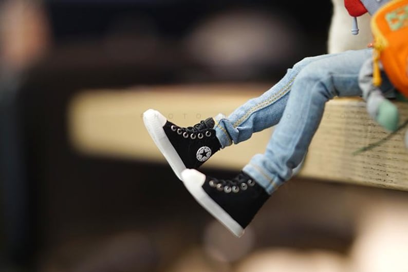 May include: A pair of black canvas high-top sneakers with white soles and a white star logo. The sneakers are worn by a person wearing blue jeans.