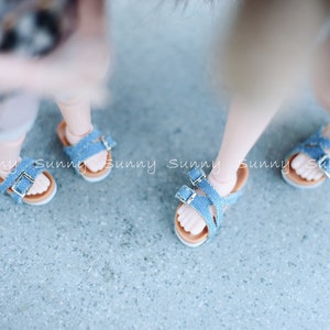 May include: Two pairs of blue denim sandals with adjustable straps and buckles. The sandals have a brown leather sole.