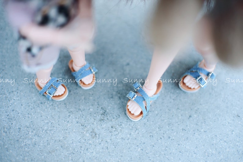 May include: Two pairs of blue denim sandals with adjustable straps and buckles. The sandals have a brown leather sole.