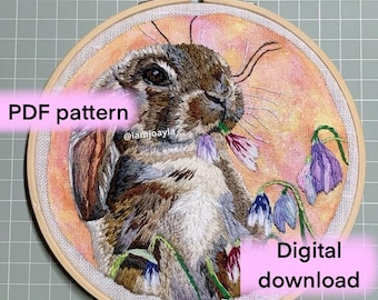 May include: A digital download PDF pattern for an embroidery project featuring a brown rabbit with a pink flower in its mouth and blue flowers in the background. The pattern is available for instant download.