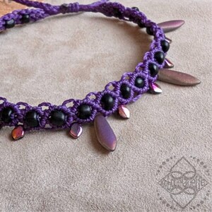 Könnte beinhalten: Eine violette und schwarze Perlenkette mit schillernden violetten und schwarzen tropfenförmigen Anhängern.