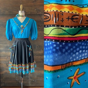 May include: A vintage turquoise blouse with a black and turquoise trim and a black skirt with a colourful southwestern print trim. The skirt has two pockets with ties.