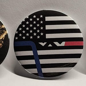 May include: Three round pinback buttons. One button features a map of the United States with the word "HELP" in illuminated text. Another button displays a stylized American flag with a blue line and a red line. The third button depicts the Statue of Liberty with the word "HELP" on her back.