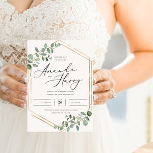 May include: A wedding invitation featuring the names "Amanda" and "Harry" in elegant script. The invitation has a gold geometric frame with watercolor eucalyptus leaves. The date is August 26, 2021, at 3 o'clock. The invitation is held by a person wearing a white dress.