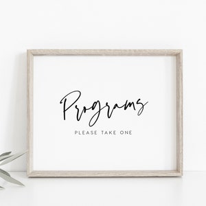May include: A white framed sign with black text that reads "Programs" in cursive script and "Please take one" in a sans-serif font.