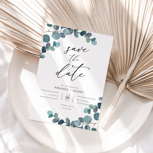 Op de afbeelding: Een witte 'Save the Date'-kaart met elegant schrift en eucalyptusaccenten. De kaart bevat de namen Amanda en Harry, de datum 26 augustus 2021 en de locatie Melbourne. Het ontwerp toont elementen in aquarel.