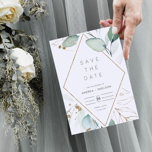 Op de afbeelding: Een witte save-the-date kaart met gouden en groene accenten. De kaart heeft een geometrisch ontwerp met de tekst "Save the Date" en de namen "Andrea + Sheldon". De datum is zaterdag 26 augustus 2021 in Melbourne.