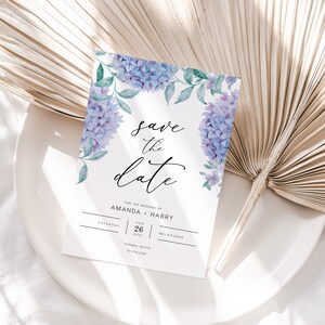 May include: Save the date card with watercolor purple flowers and greenery. The card says "Save the date" for the wedding of Amanda and Harry on Saturday, August 26, 2021 in Melbourne.