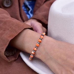 May include: A bracelet with orange and silver beads. The bracelet is on a person's wrist.