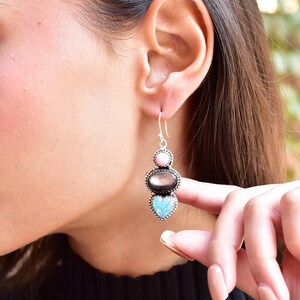 May include: Silver dangle earrings with a heart-shaped blue opal stone, a black oval stone, and a pink oval stone.