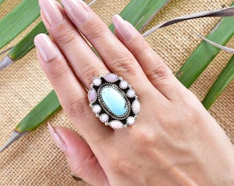 May include: A turquoise and pink oval ring with a silver setting. The ring is set with a large turquoise stone surrounded by smaller pink and white stones.