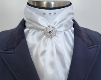 May include: A white satin stock tie with a silver rhinestone brooch. The tie is worn with a navy blue jacket.