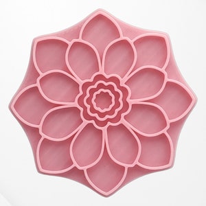 Könnte beinhalten: Eine rosa Silikonform in Form einer Blume mit mehreren Blütenblättern und einem Mittelkreis. Die Form ist für die Herstellung von Dekorationsartikeln wie Seife, Harz oder Ton gedacht.