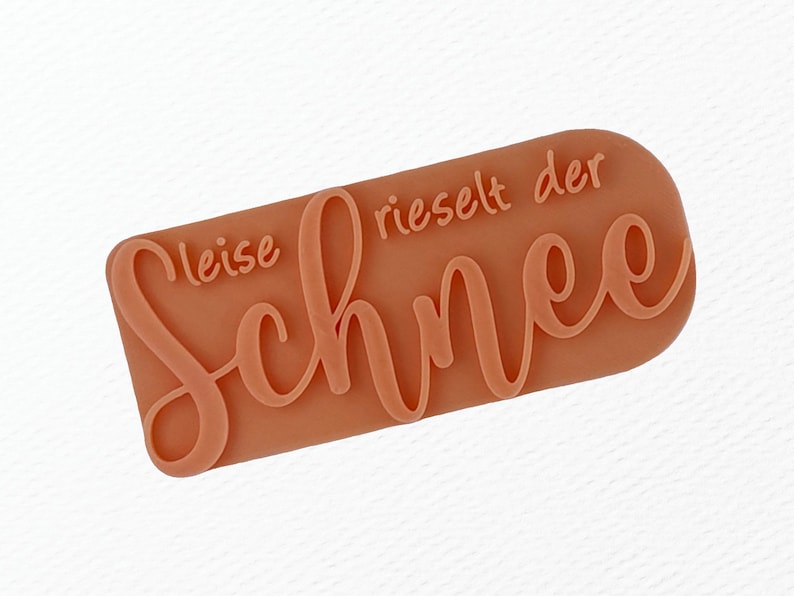 May include: A light brown rubber stamp with the text "leise rieselt der Schnee" in a cursive font.