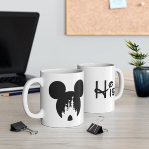 May include: Two white ceramic mugs with black designs. One mug features a silhouette of Mickey Mouse's head with the iconic Disney castle inside the ear. The other mug has the word "His" written in a stylized font.