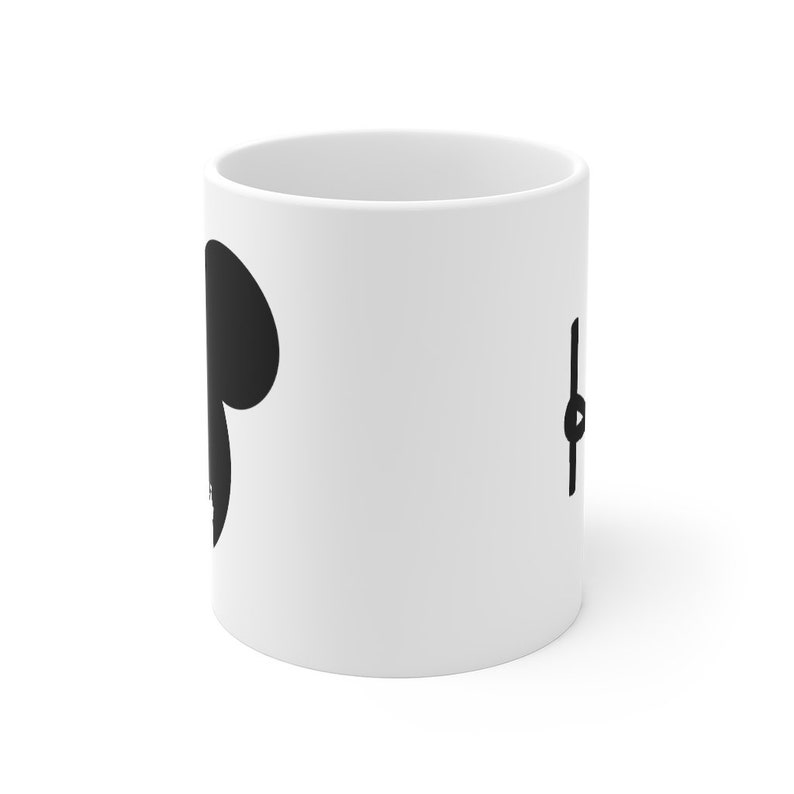 May include: White ceramic mug with a black silhouette of a mouse head on one side and a black play button on the other side.