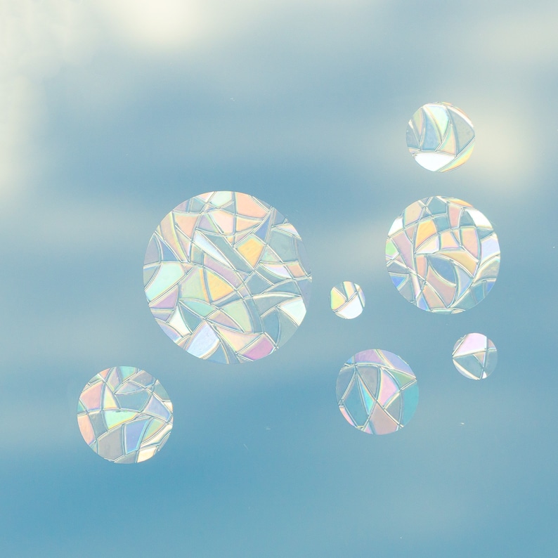 May include: Iridescent, stained-glass-style circular decals in various sizes. The decals are composed of geometric shapes in pastel colors, creating a rainbow effect. They are set against a light blue background, resembling a sky.