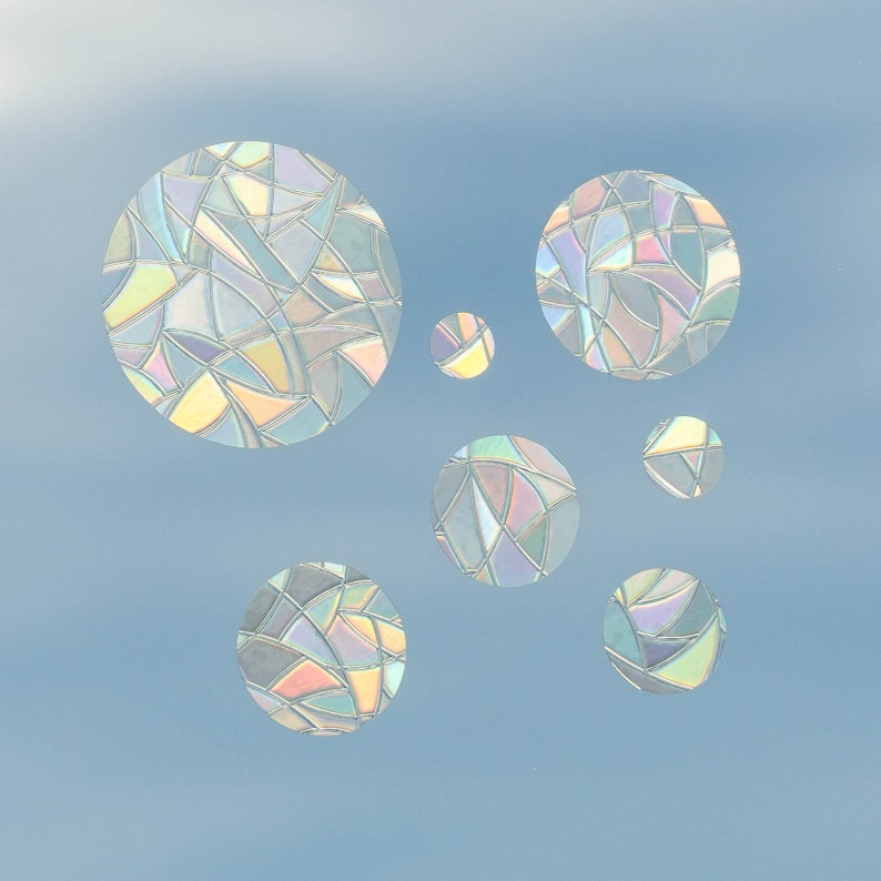 May include: Seven iridescent, stained-glass-style circular window clings against a light blue background. The circles vary in size and feature a mosaic pattern of geometric shapes in a range of colors, including blue, green, yellow, and pink.