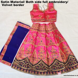 May include: A pink satin lehenga with gold and blue embroidery, a matching pink satin choli with gold and blue embroidery, and a blue satin dupatta with gold embroidery. The lehenga has a velvet border.
