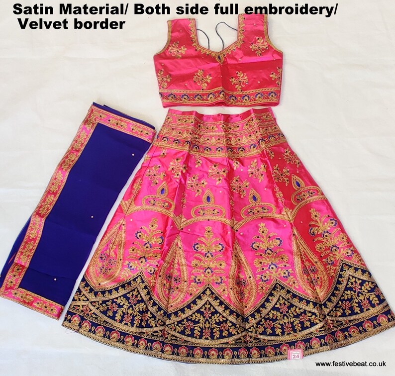 May include: A pink satin lehenga with gold and blue embroidery, a matching pink satin choli with gold and blue embroidery, and a blue satin dupatta with gold embroidery. The lehenga has a velvet border.