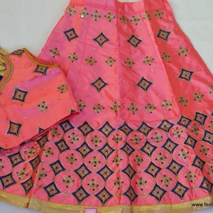 May include: A pink and blue embroidered skirt and matching top with gold trim. The skirt has a diamond pattern and the top has a V-neck.