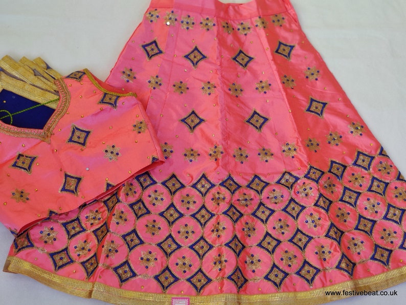 May include: A pink and blue embroidered skirt and matching top with gold trim. The skirt has a diamond pattern and the top has a V-neck.