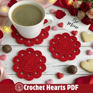 May include: A white mug filled with a green beverage sits on a red crocheted coaster. Two additional red coasters are visible, along with heart-shaped candies, chocolates, and a card that says "Be Mine". The image is themed around Valentine's Day.