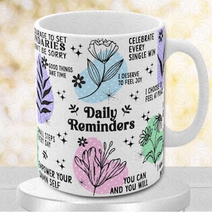 Puede incluir: Taza de cerámica blanca con un diseño colorido que incluye flores, estrellas y frases inspiradoras. El texto incluye "Daily Reminders", "Celebrate Every Single Win", "I Deserve to Feel Joy", "I Choose to Feel at Peace", "Courage to Set Boundaries", "Don't Be Sorry", "Good Things Take Time", "Small Steps Every Day", "Empower Your Damn Self", "You Can and You Will".