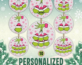 May include: Round white Christmas ornaments featuring a green hand wearing a pink cuff holding multiple green characters in Santa hats. The background has pink snowflakes. One ornament displays the text MOM. The ornaments hang from twine strings.