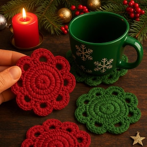 Könnte beinhalten: Nahaufnahme von roten und grünen gehäkelten Untersetzern auf einer Holzoberfläche. Eine Hand hält einen roten Untersetzer. Eine grüne Tasse mit Schneeflockenmustern steht auf einem grünen Untersetzer. Eine brennende rote Kerze und Weihnachtsdekorationen im Hintergrund.