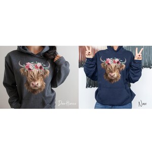 Puede incluir: Dos sudaderas con capucha con un gr&aacute;fico de vaca Highland coronada con flores. La sudadera de la izquierda es de color gris oscuro y la sudadera de la derecha es de color azul marino. El texto "Dark Heather" est&aacute; debajo de la sudadera de la izquierda y el texto "Navy" est&aacute; debajo de la sudadera de la derecha.